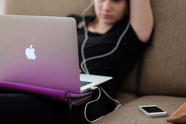 Person listening to music on a MacBook with wired earplugs
