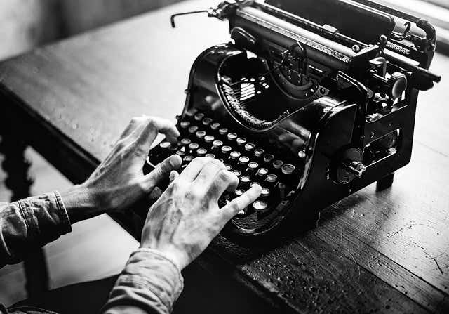 Black & white image of a man typing on an antique typewriter