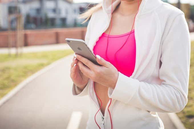 Photo of woman from the neck down 
 wearing red wired earbuds and holding iPhone 