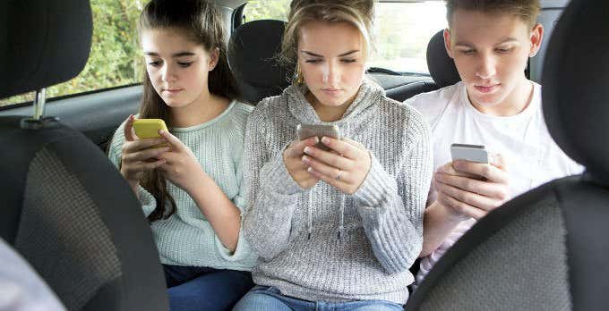 Three young people in the back seat of a car on iPhones 