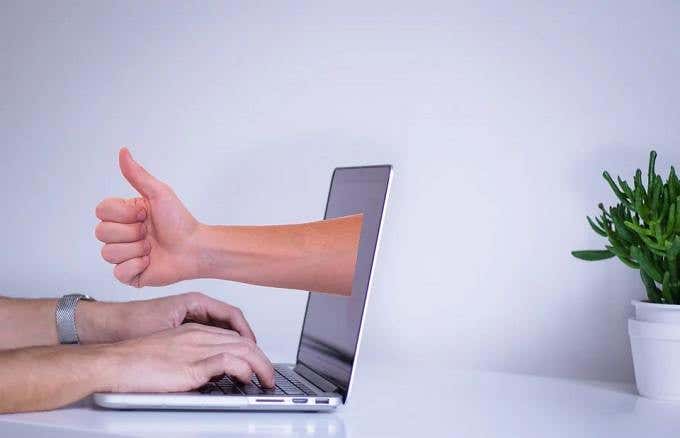 Someone's thumbs up protruding from a a laptop 
