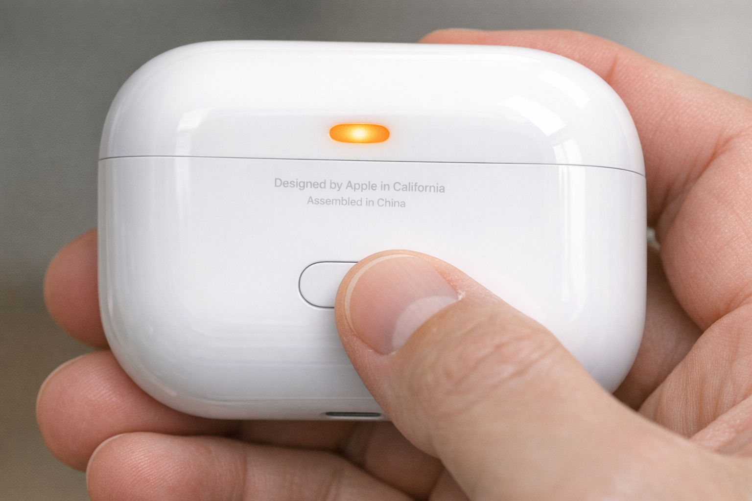 Hand pressing and holding the setup button on the back of an AirPods charging case, with the LED visible on the front of the case